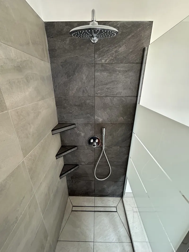 Douche à l'italienne aux grands carreaux gris, avec étagères d'angle