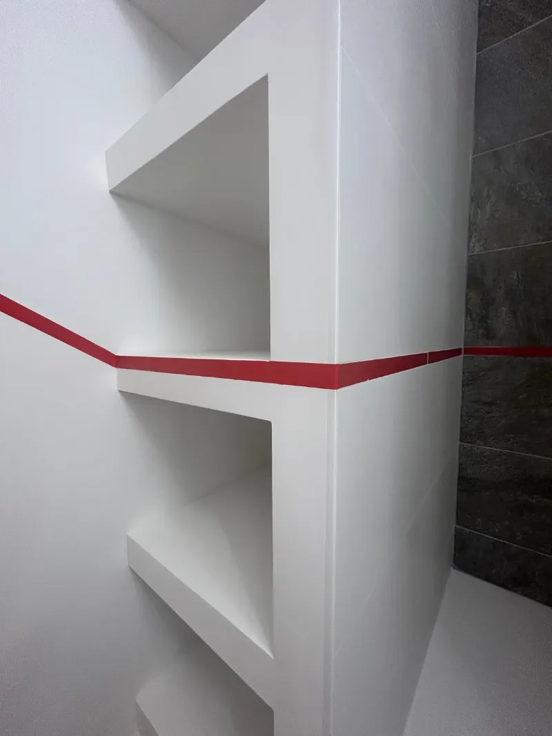 Niches maçonnées dans un mur blanc, aux angles nets, à côté d'une douche carrelée